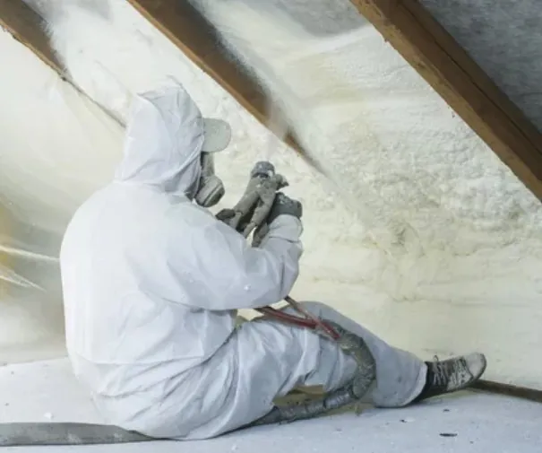Applicator spraying closed-cell foam on an attic roof deck