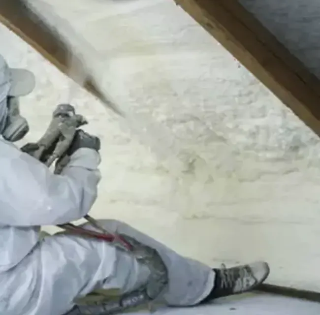Applicator spraying closed-cell foam on a sloped roof deck