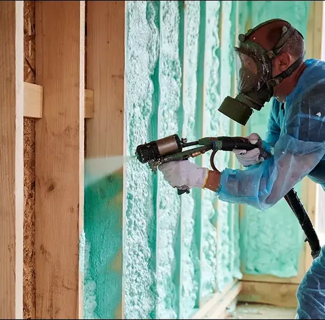 Applicator spraying closed-cell foam into framing