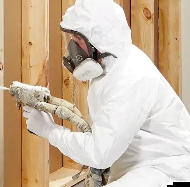 Applicator spraying foam into framed walls